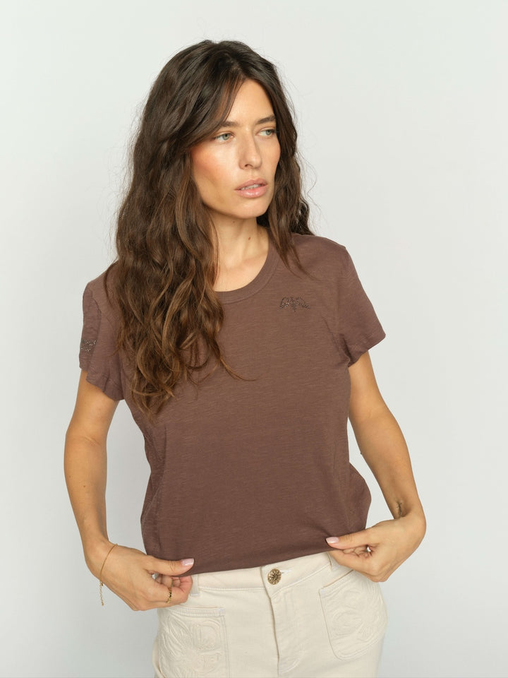 Mos Mosh Woman wearing a brown t-shirt against a plain studio background