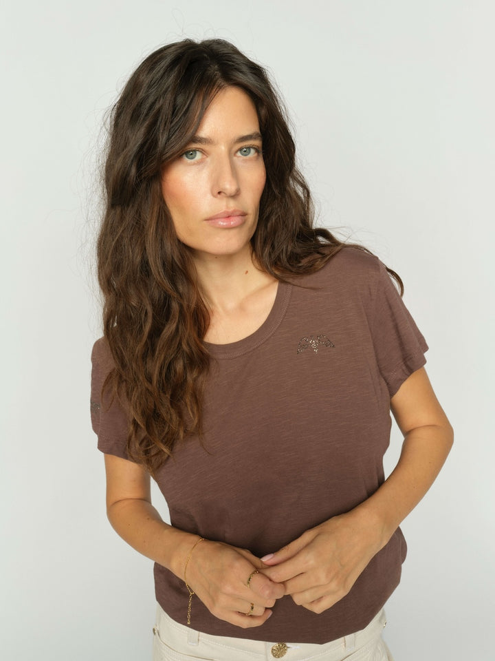 Mos Mosh Woman wearing a brown t-shirt against a plain studio background