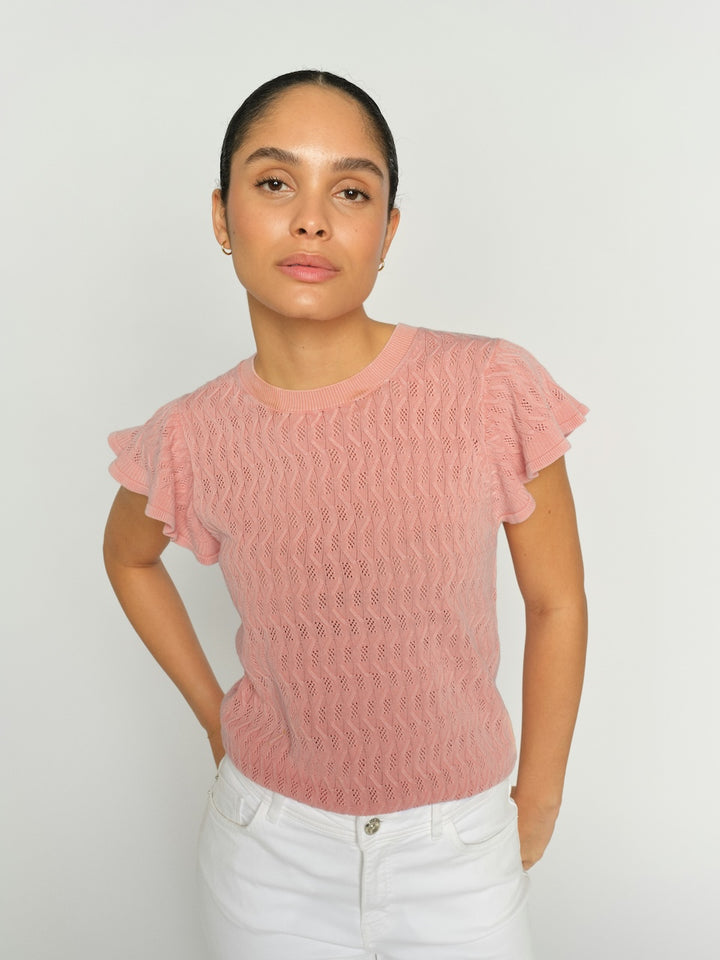 Woman wearing a pink textured top against a plain background