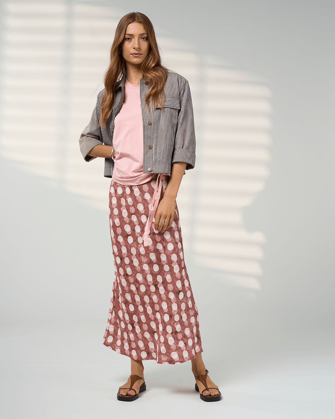 Madly Sweetly model in a pink midi skirt with allover white dot print and elastic gathered waist. On a studio background