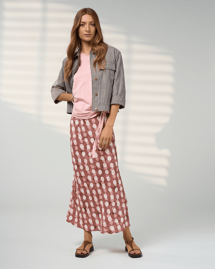 Madly Sweetly model in a pink midi skirt with allover white dot print and elastic gathered waist. On a studio background
