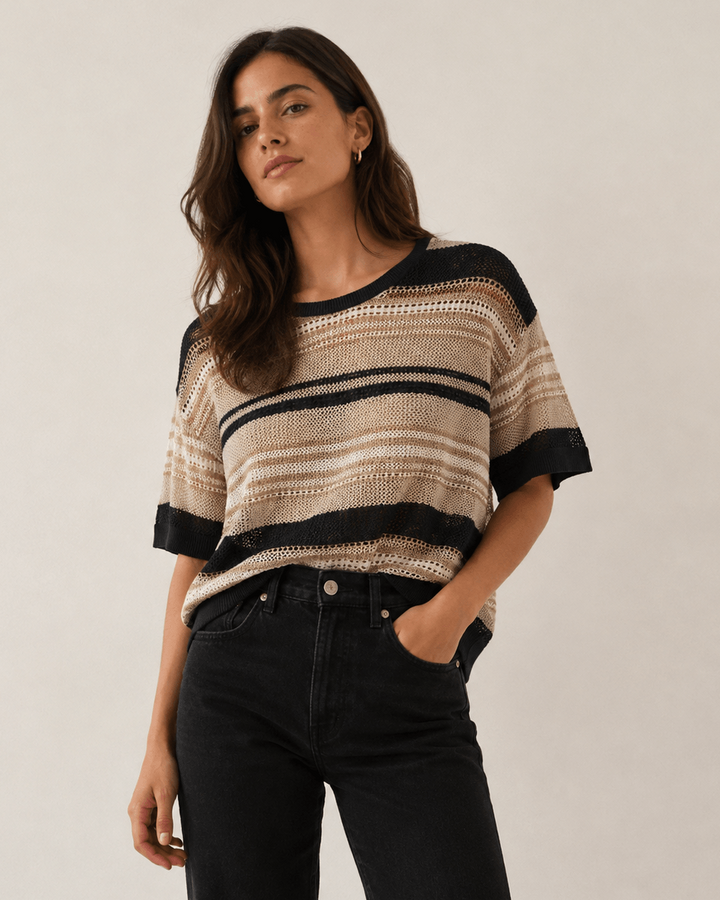 LD&amp;Co modeling wearing a short-sleeve knit sweater with horizontal beige, brown, and black stripes, paired with black jeans, against a plain light beige studio background.