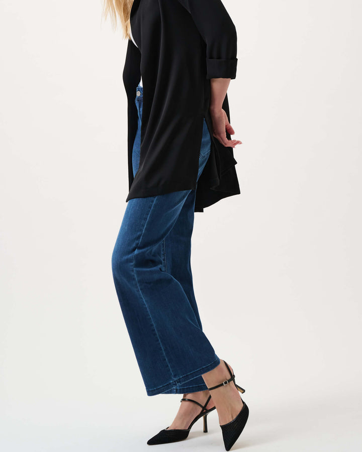 Joseph Ribkoff  model wearing a black long-sleeve open-front cardigan, blue wide-leg jeans, and black pointed-toe heels, standing against a plain white studio background.