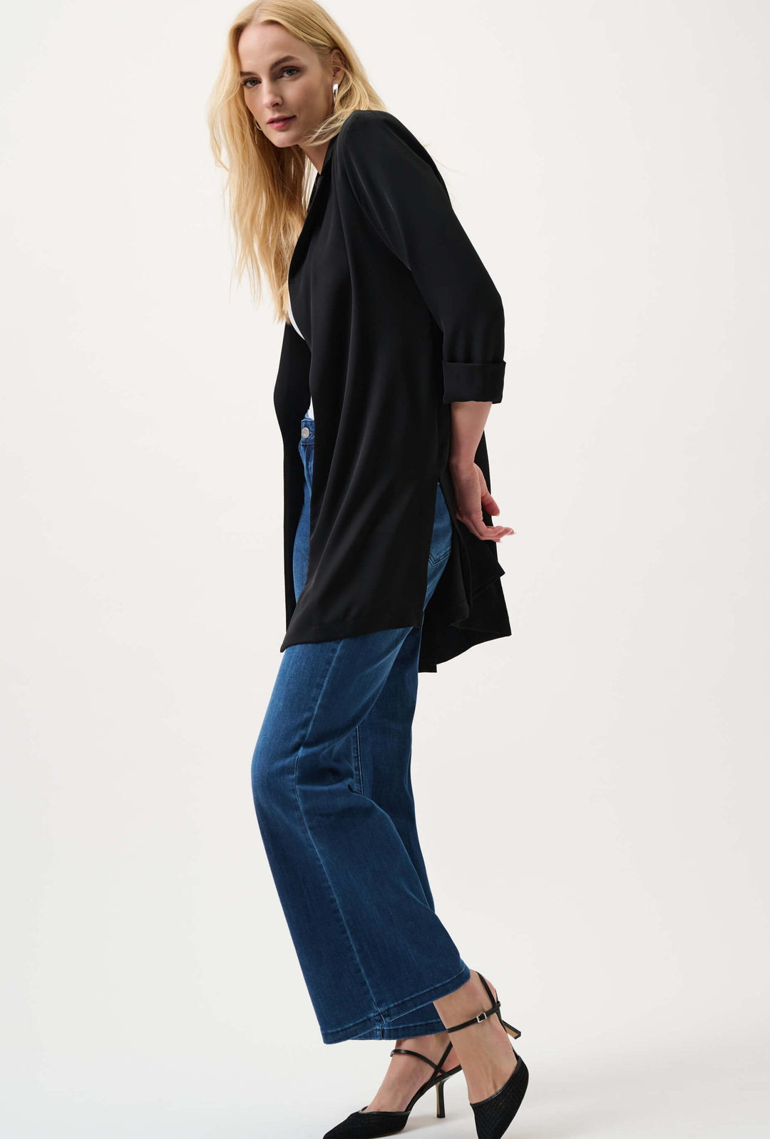 Joseph Ribkoff  model wearing a black long-sleeve open-front cardigan, blue wide-leg jeans, and black pointed-toe heels, standing against a plain white studio background.