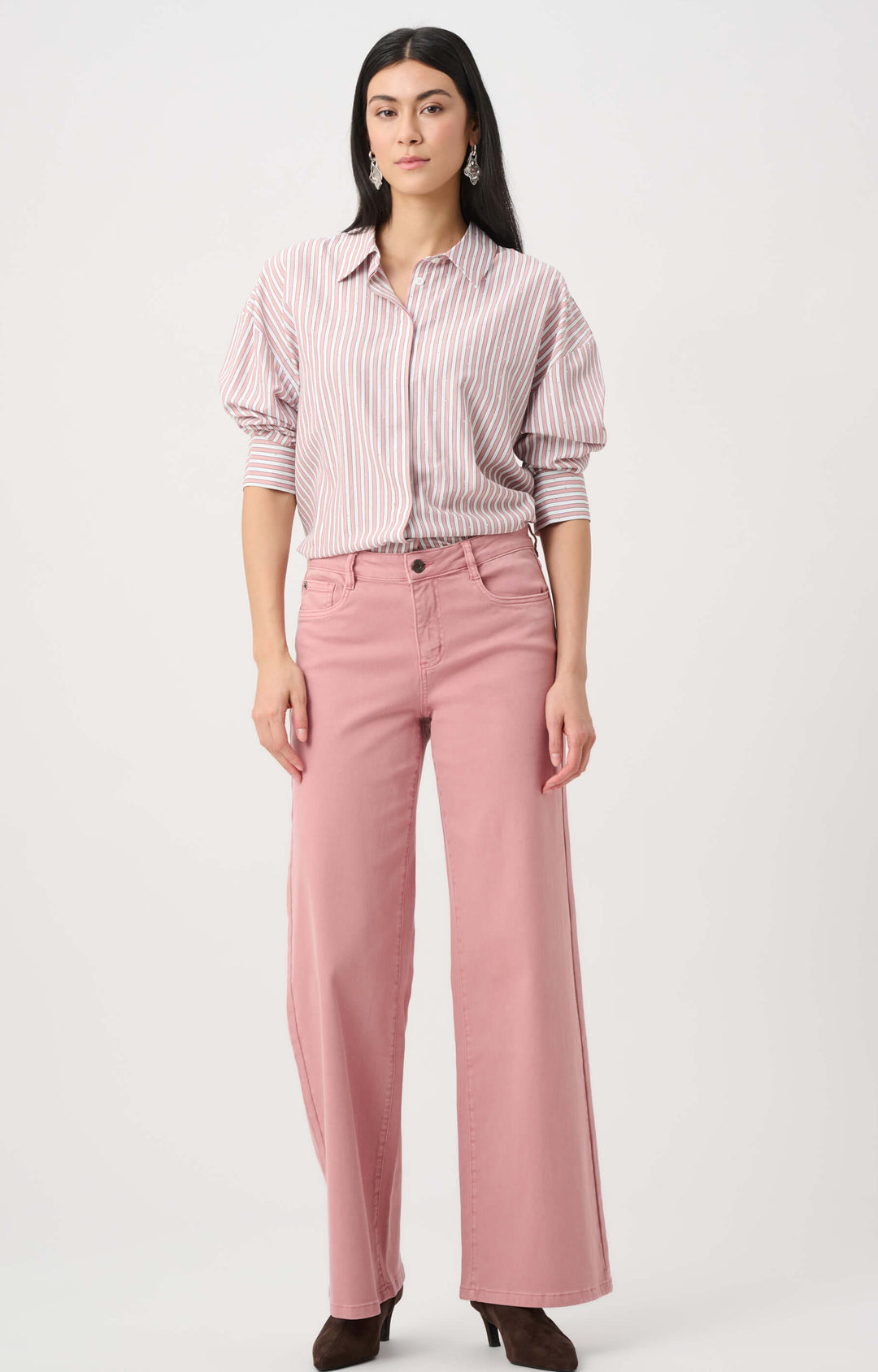 Joseph Ribkoff modeling a pink and white vertically striped button-down shirt with puffed sleeves, paired with dusty pink wide-leg pants and dark brown pointed-toe heels, against a plain light gray studio background.