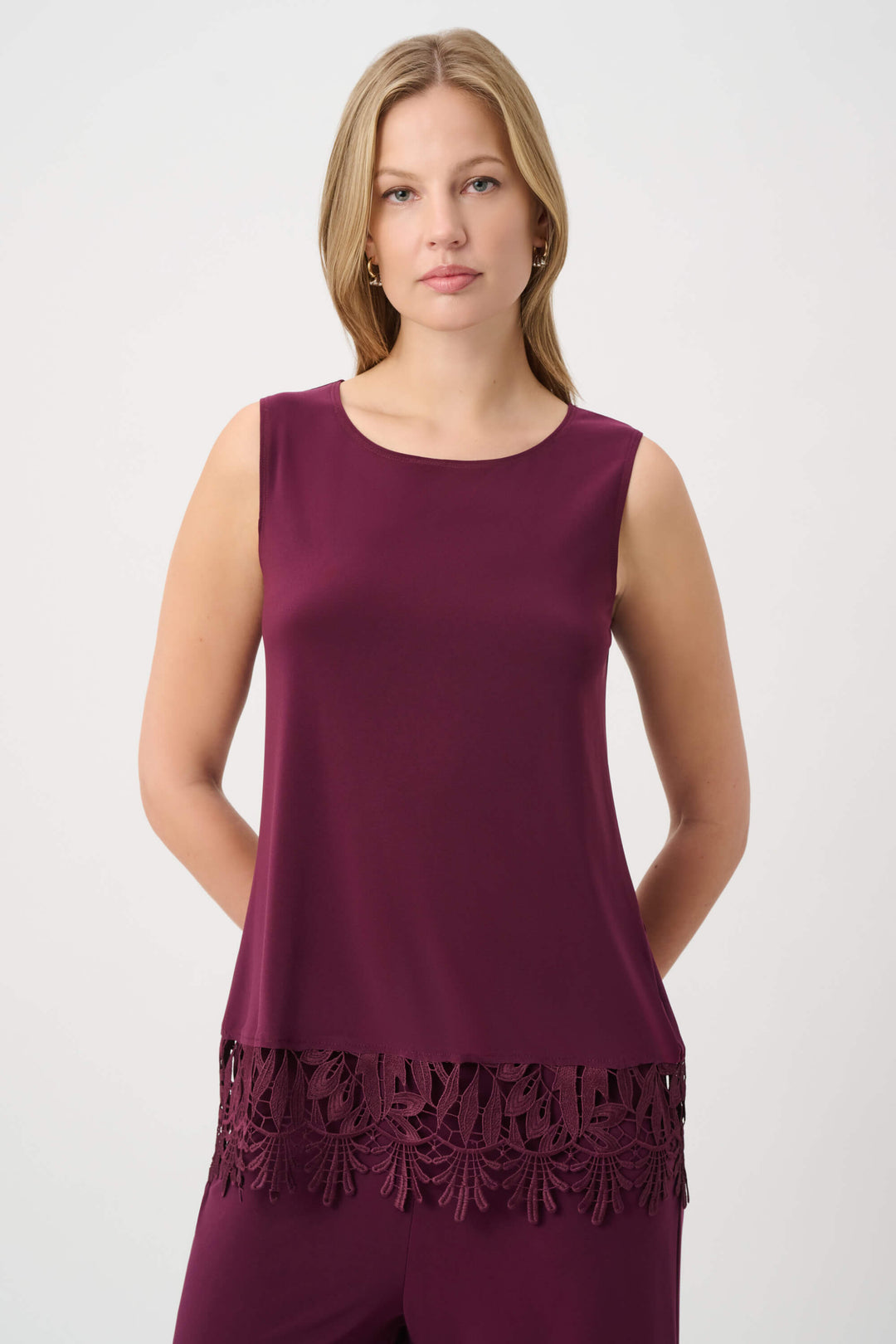 Joseph Ribkoff modeling a sleeveless scoop-neck top in deep burgundy with a matching lace-trimmed hem, paired with matching pants, against a plain light gray studio background.