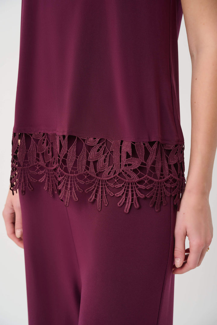 Joseph Ribkoff modeling a sleeveless scoop-neck top in deep burgundy with a matching lace-trimmed hem, paired with matching pants, against a plain light gray studio background. Close up