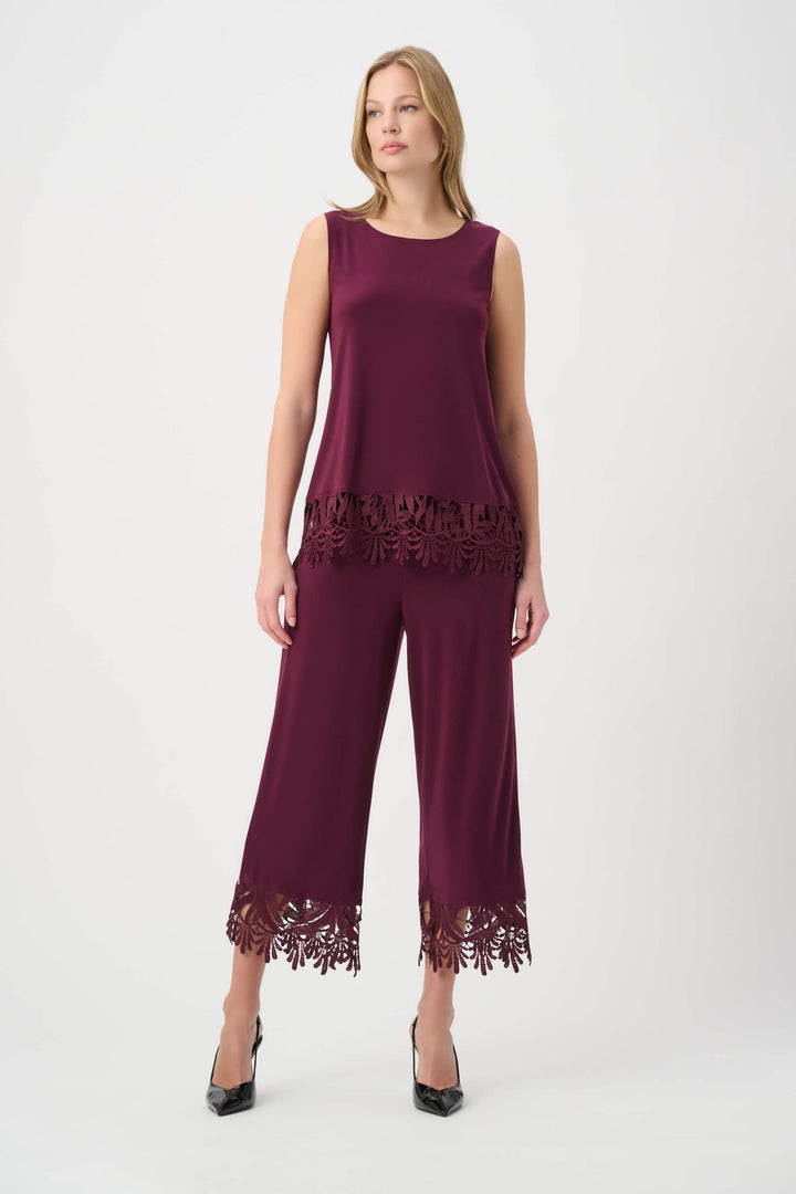 Joseph Ribkoff modeling a sleeveless scoop-neck top in deep burgundy with a matching lace-trimmed hem, paired with matching pants, against a plain light gray studio background.
