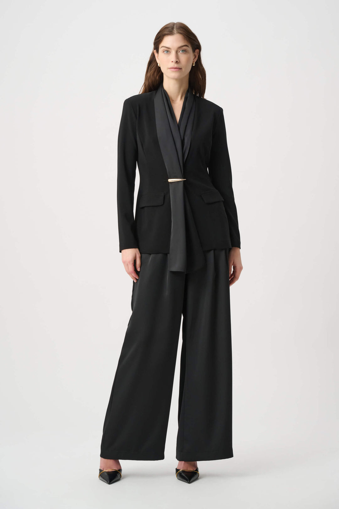 Joseph Ribkoff model wearing black wide-leg cropped trousers with a high waist and front pleats, paired with black pointed-toe heels against a light gray studio background.