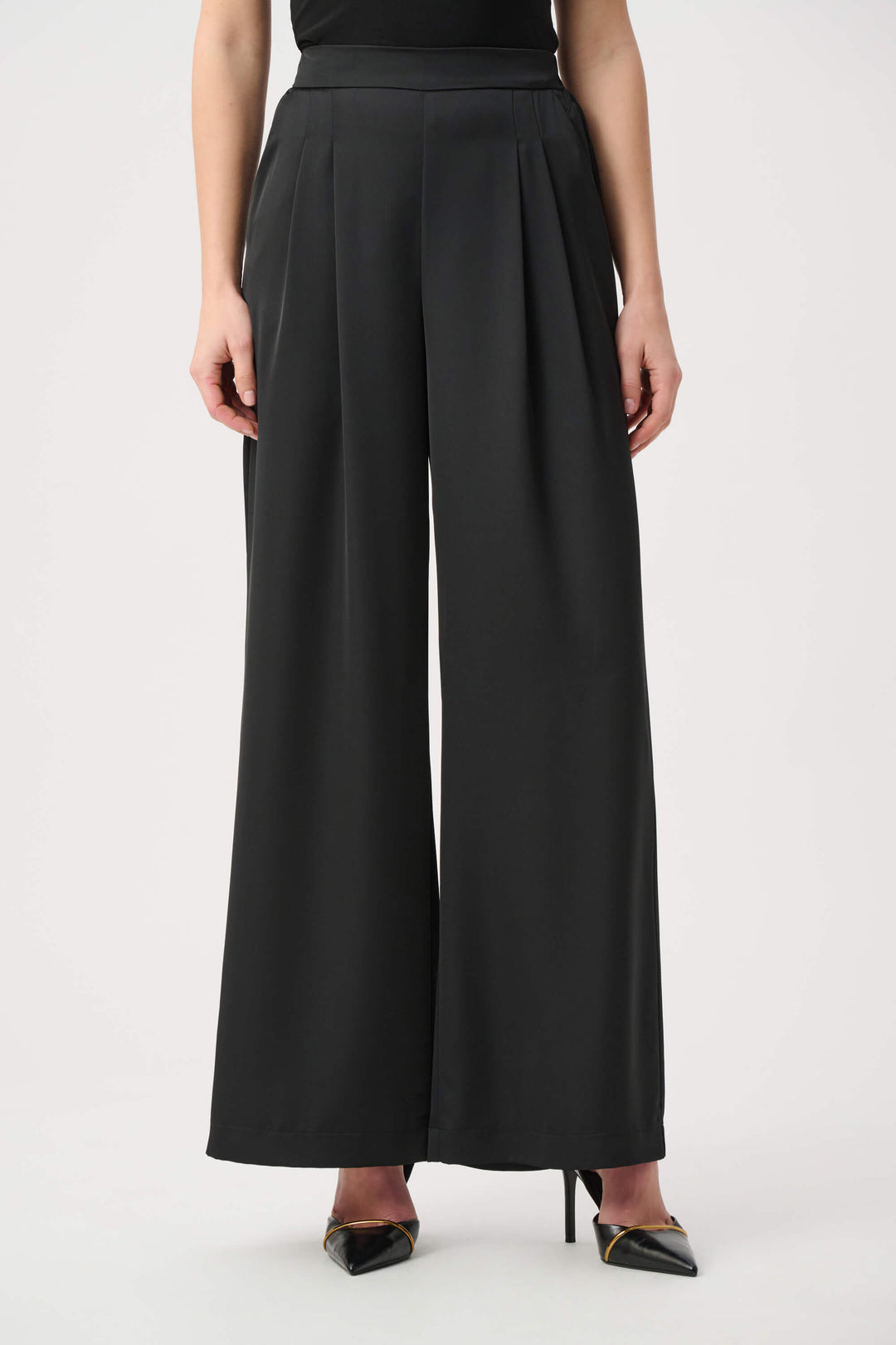 Joseph Ribkoff model wearing black wide-leg cropped trousers with a high waist and front pleats, paired with black pointed-toe heels against a light gray studio background.