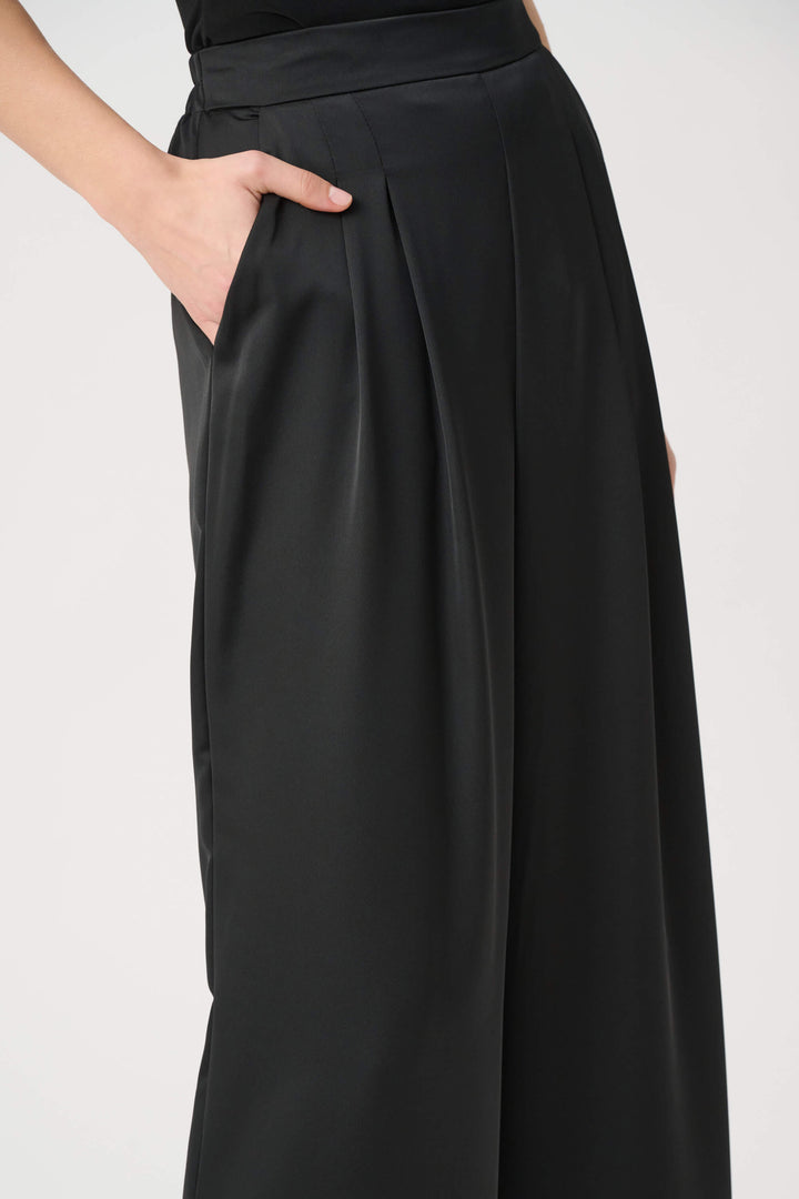 Joseph Ribkoff model wearing black wide-leg cropped trousers with a high waist and front pleats, paired with black pointed-toe heels against a light gray studio background. Close up
