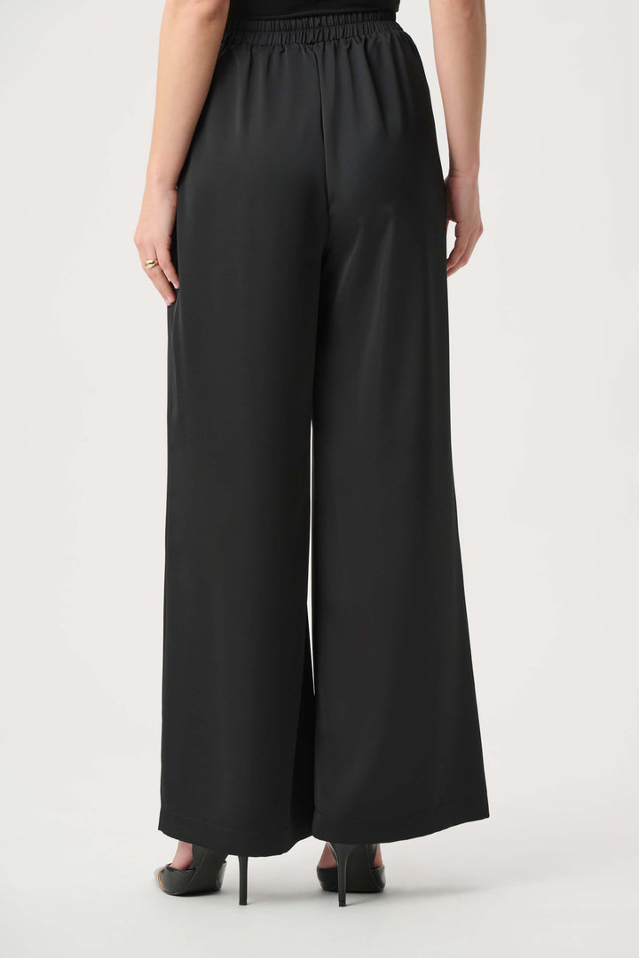 Joseph Ribkoff model wearing black wide-leg cropped trousers with a high waist and front pleats, paired with black pointed-toe heels against a light gray studio background. Back view