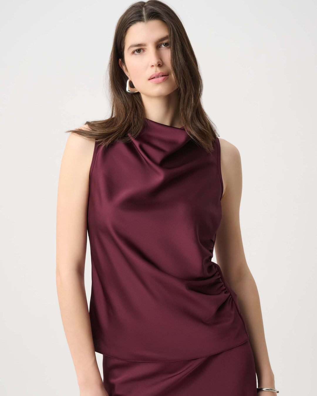 Joseph Ribkoff  modeling a sleeveless, high-neck, draped satin dress in a deep burgundy color against a plain light gray background.