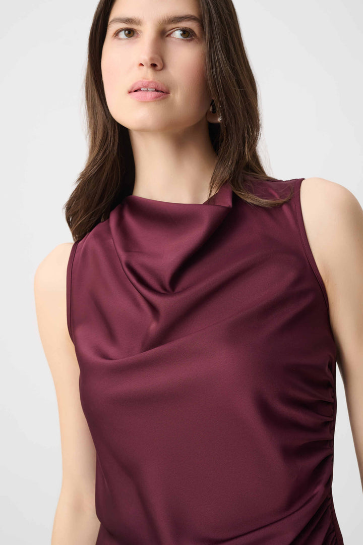 Joseph Ribkoff  modeling a sleeveless, high-neck, draped satin dress in a deep burgundy color against a plain light gray background.