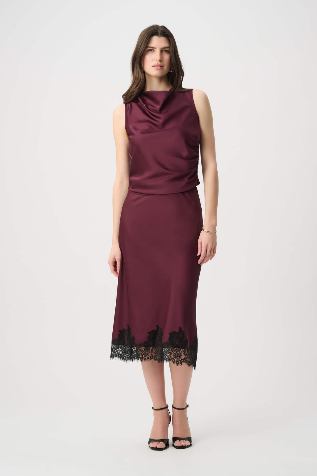 Joseph Ribkoff  modeling a sleeveless, high-neck, draped satin dress in a deep burgundy color against a plain light gray background.