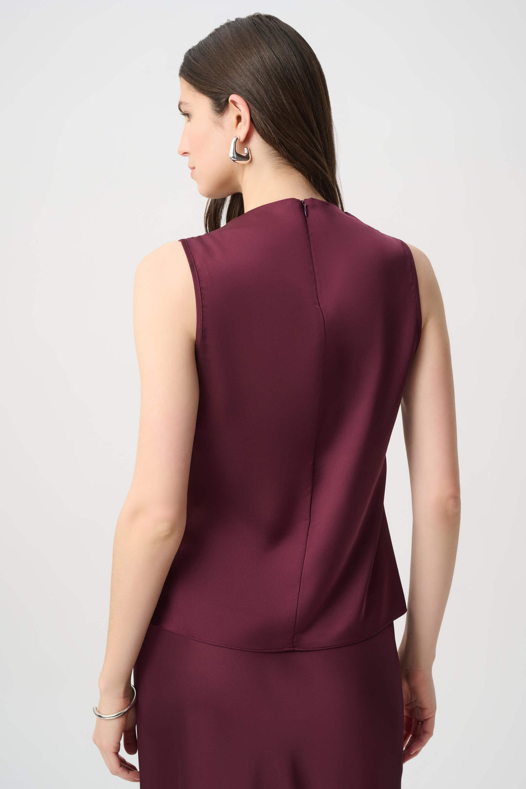 Joseph Ribkoff  modeling a sleeveless, high-neck, draped satin dress in a deep burgundy color against a plain light gray background back view 