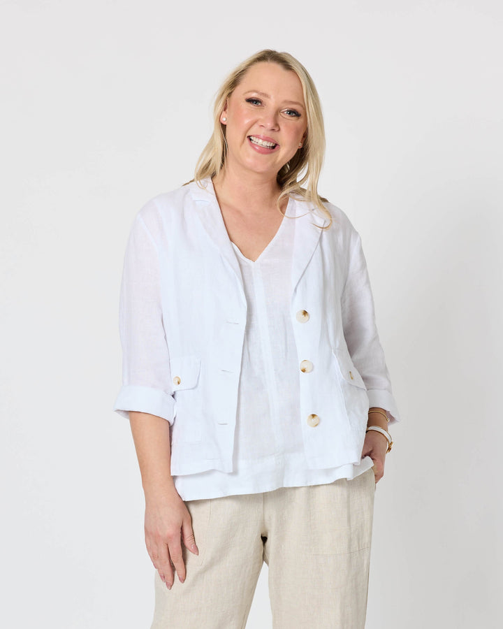 Gordon Smith  modeling a white button-up linen jacket and beige linen trousers, standing against a plain white studio background.