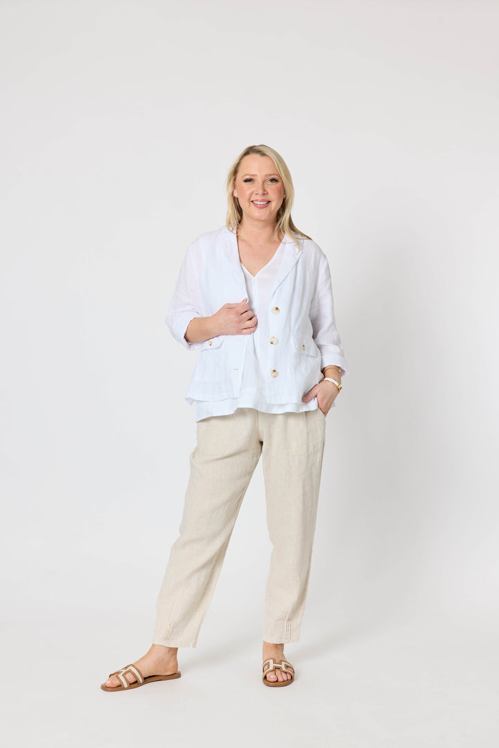 Gordon Smith  modeling a white button-up linen jacket and beige linen trousers, standing against a plain white studio background.