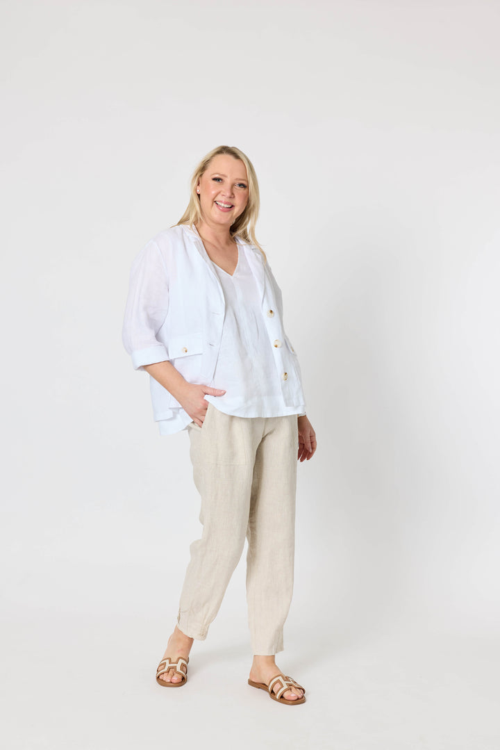 Gordon Smith  modeling a white button-up linen jacket and beige linen trousers, standing against a plain white studio background.