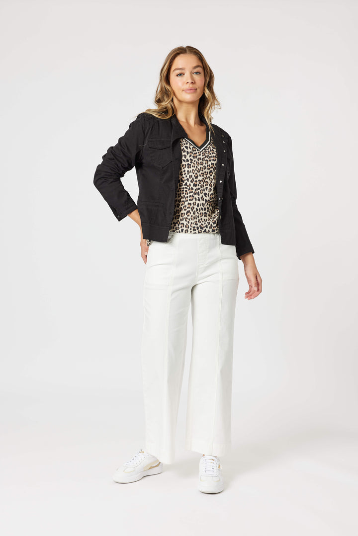 Threadz model modeling a black cropped jacket over a leopard-print top, paired with white wide-leg jeans and white sneakers, against a plain light gray studio background.