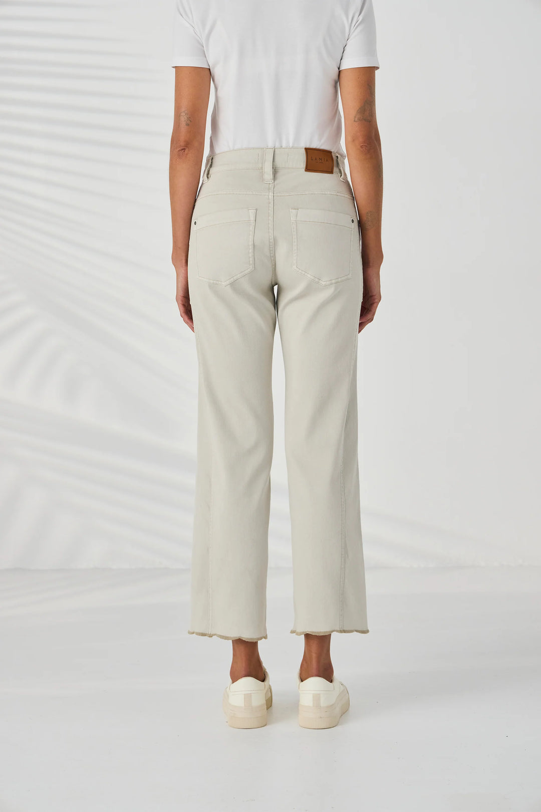 Lania The Label A model is wearing a pair of light beige cropped jeans with gold floral embroidery on the lower legs, paired with a white t-shirt and cream platform sneakers against a white studio background.