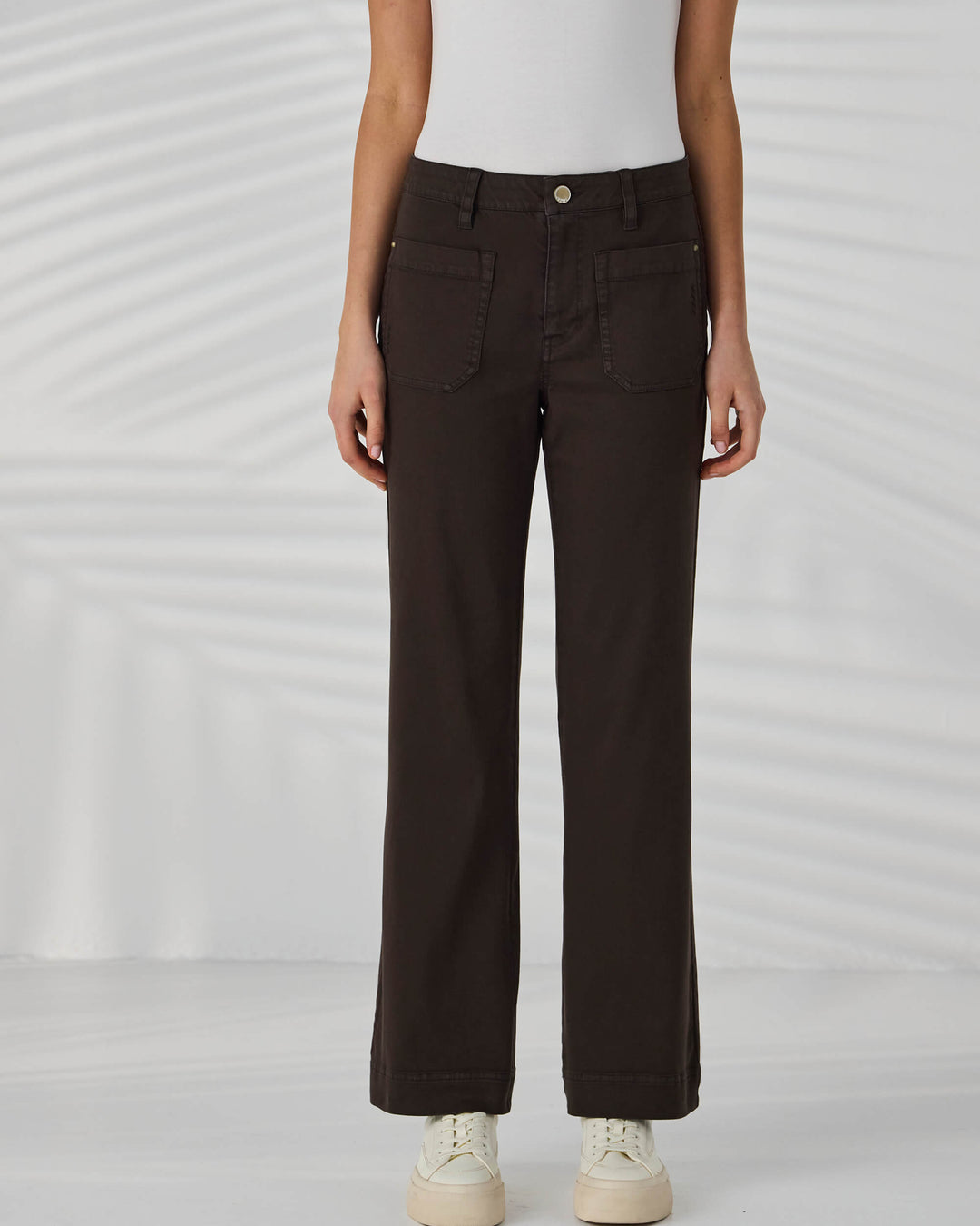 Lania The Label Model wearing black pants and white sneakers on a light gray background