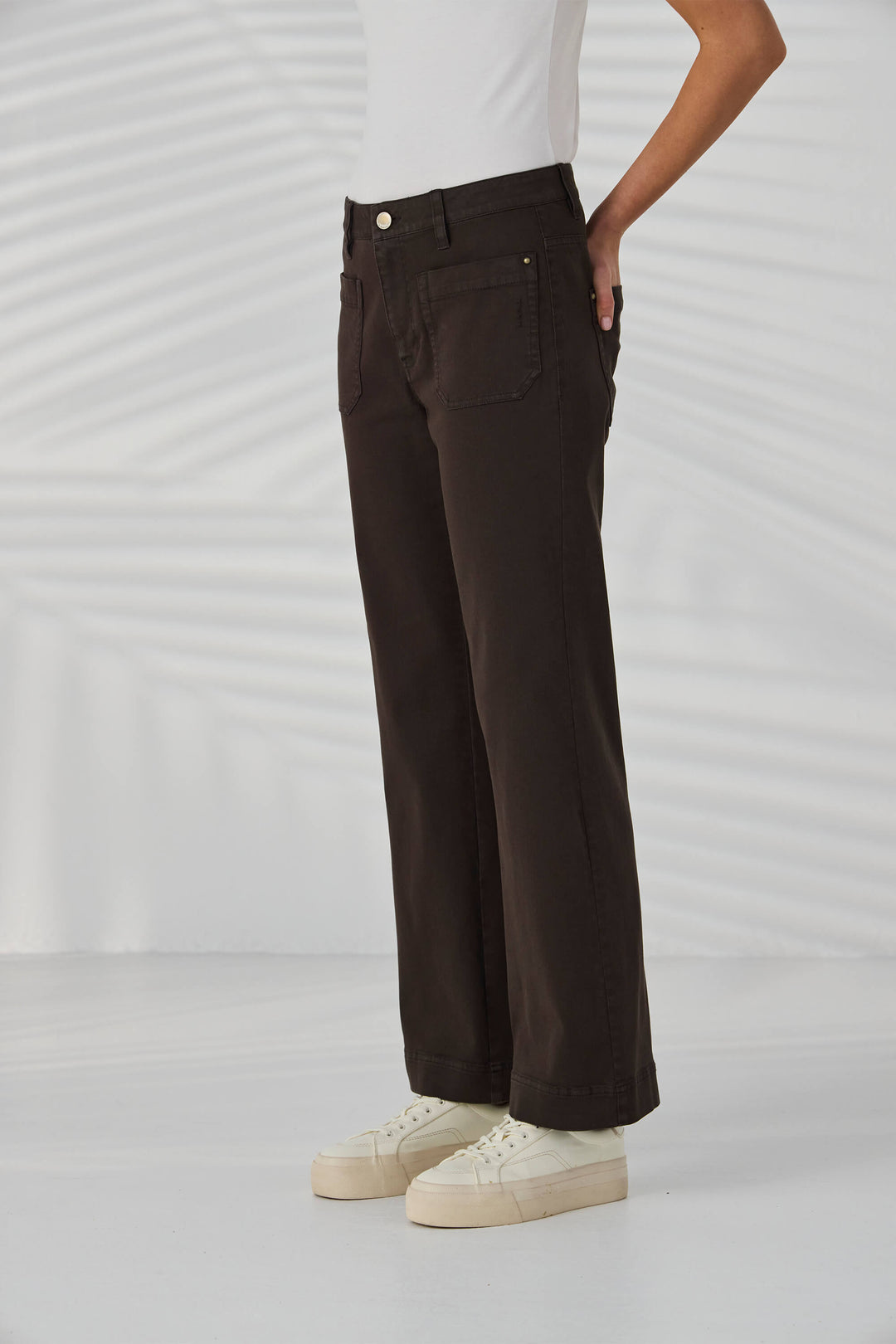 Lania The Label Model wearing dark brown pants and white sneakers on a light gray background