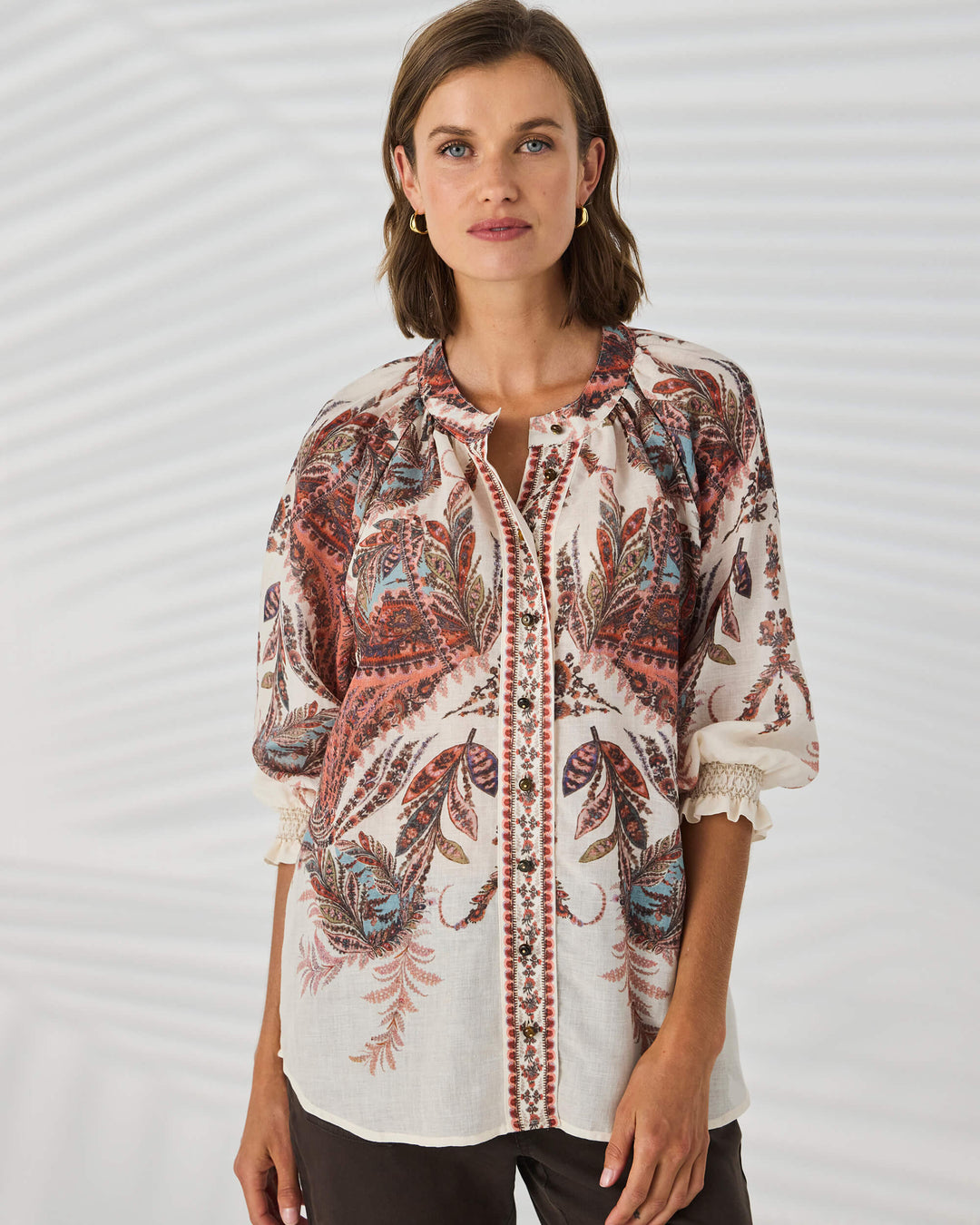 Lania The Label model wearing a loose, long-sleeve tunic top with a multicolor abstract pattern in shades of pink, beige, and brown, set against a plain white background.