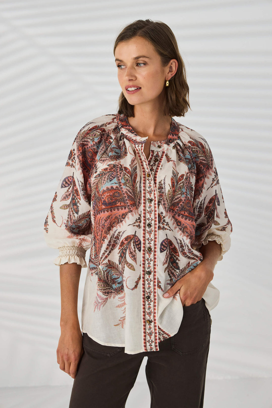 Lania The Label model wearing a loose, long-sleeve tunic top with a multicolor abstract pattern in shades of pink, beige, and brown, set against a plain white background.