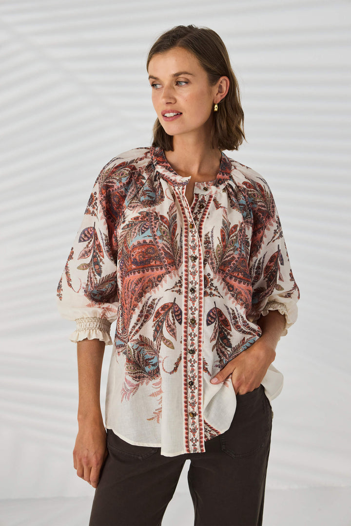 Lania The Label model wearing a loose, long-sleeve tunic top with a multicolor abstract pattern in shades of pink, beige, and brown, set against a plain white background.