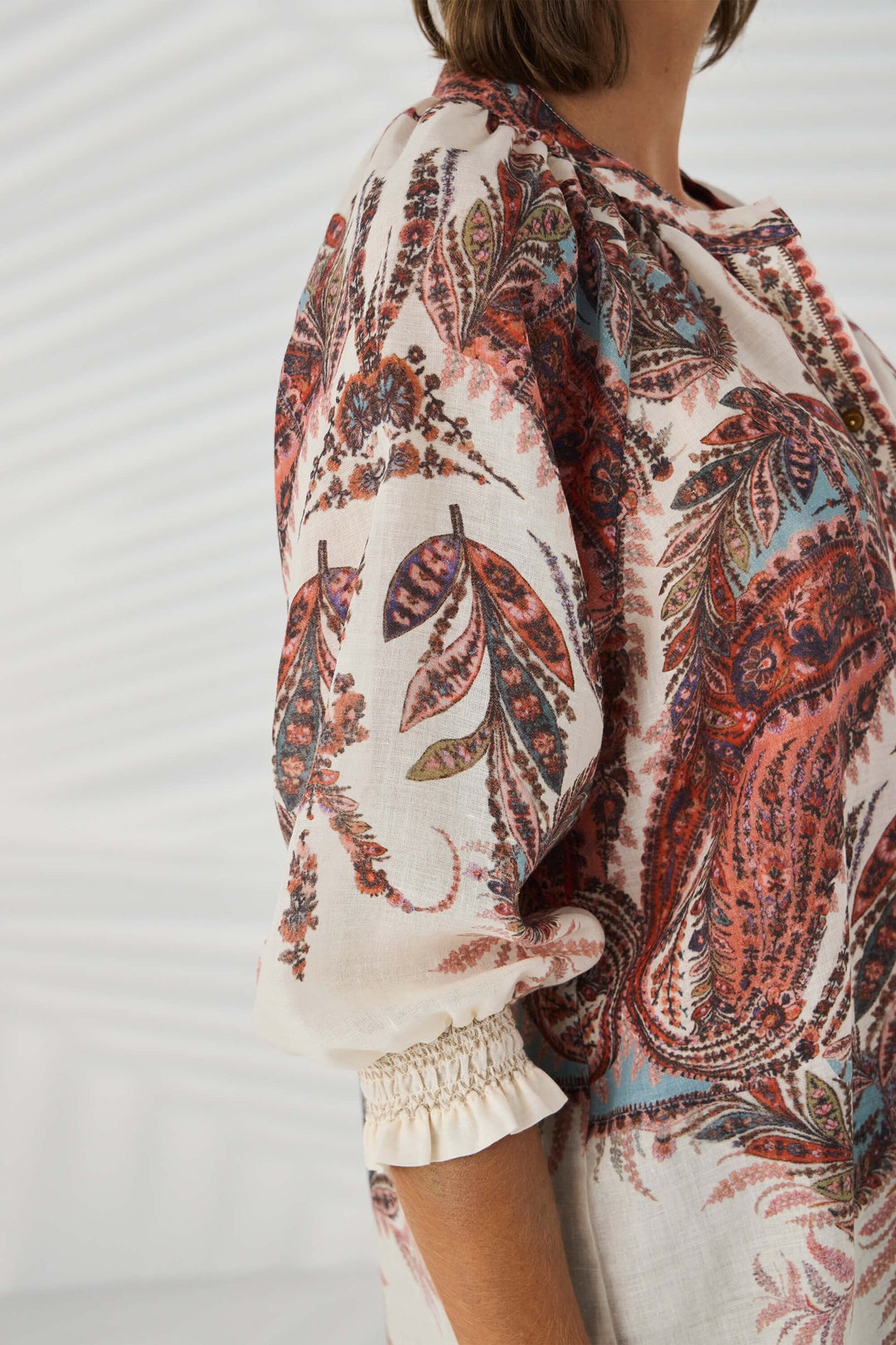 Lania The Label model wearing a loose, long-sleeve tunic top with a multicolor abstract pattern in shades of pink, beige, and brown, set against a plain white background. Close up.