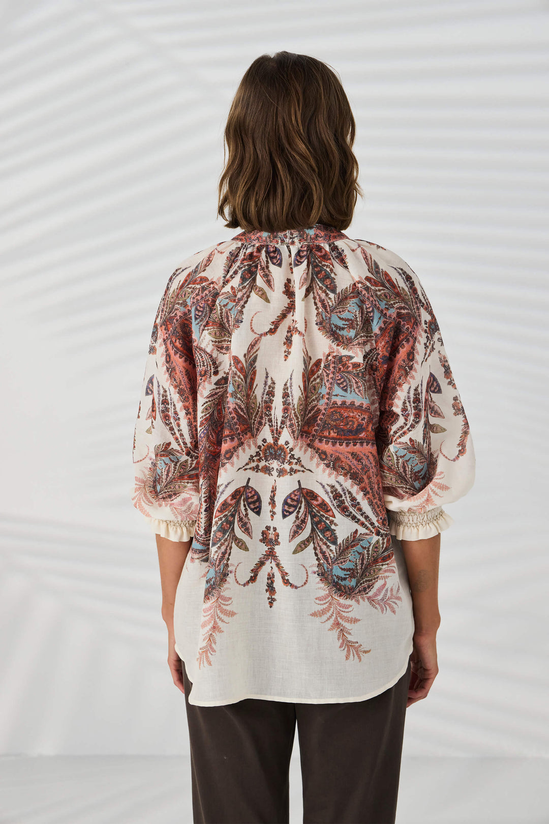 Lania The Label model wearing a loose, long-sleeve tunic top with a multicolor abstract pattern in shades of pink, beige, and brown, set against a plain white background. Back view.