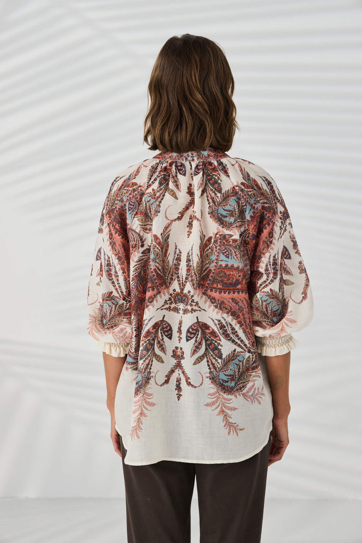 Lania The Label model wearing a loose, long-sleeve tunic top with a multicolor abstract pattern in shades of pink, beige, and brown, set against a plain white background. Back view.