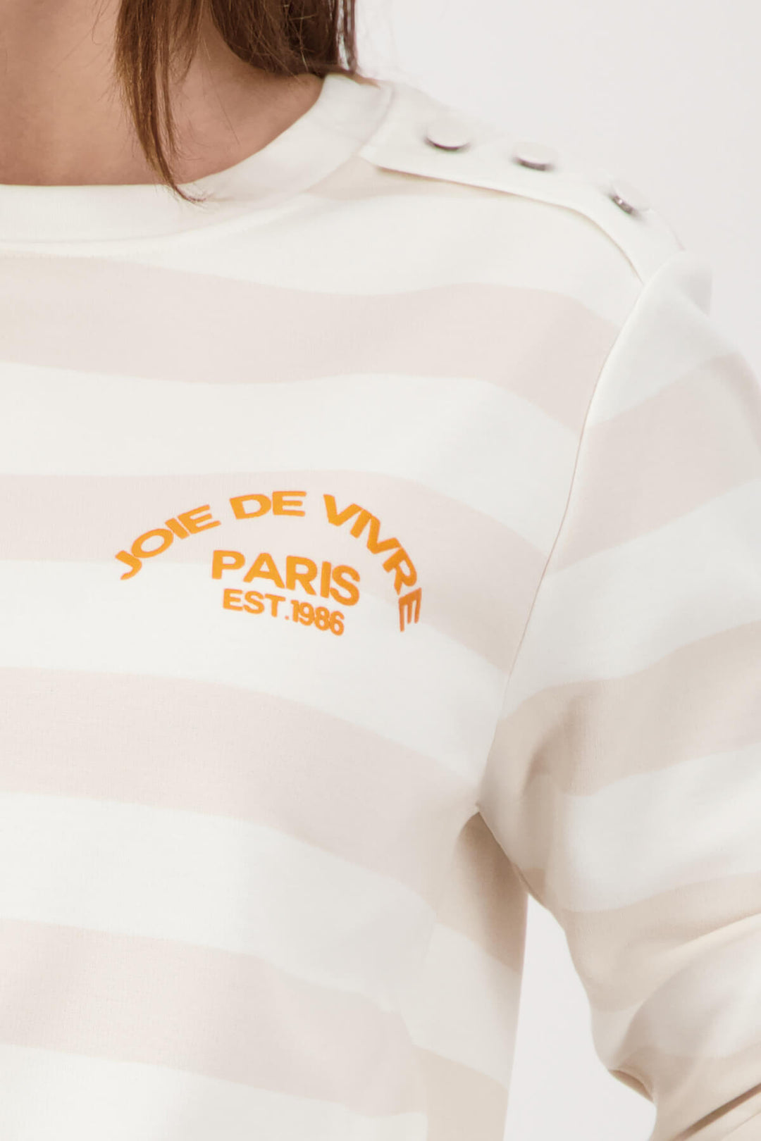 Long-sleeve jersey top detail: orange PARIS logo on light beige striped off-white fabric