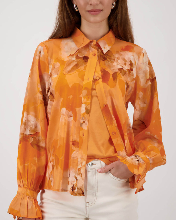 Monari orange tie-dye button-up blouse with pointed collar and long ruffle cuffs on a model