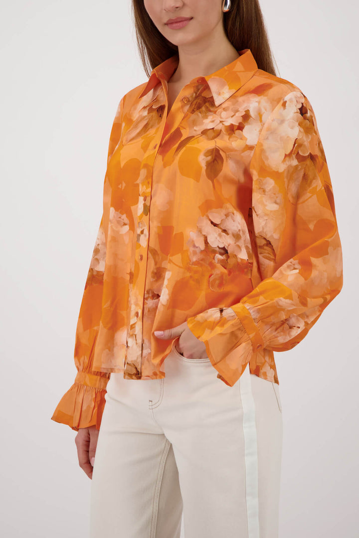 Monari orange tie-dye button-up blouse with pointed collar and long ruffle cuffs on a model