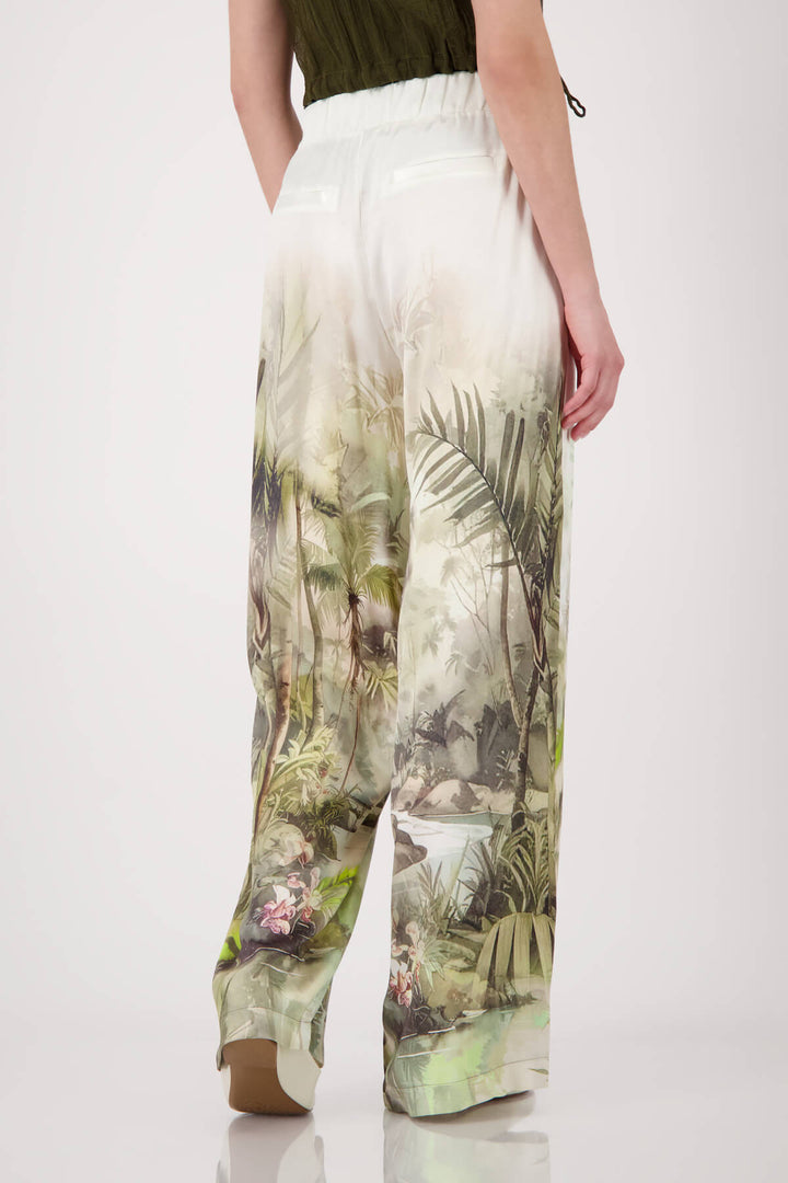 Monari woman modeling a short-sleeve olive green knit top paired with white wide-leg pants featuring a green palm tree print, set against a plain light gray studio background. Back view