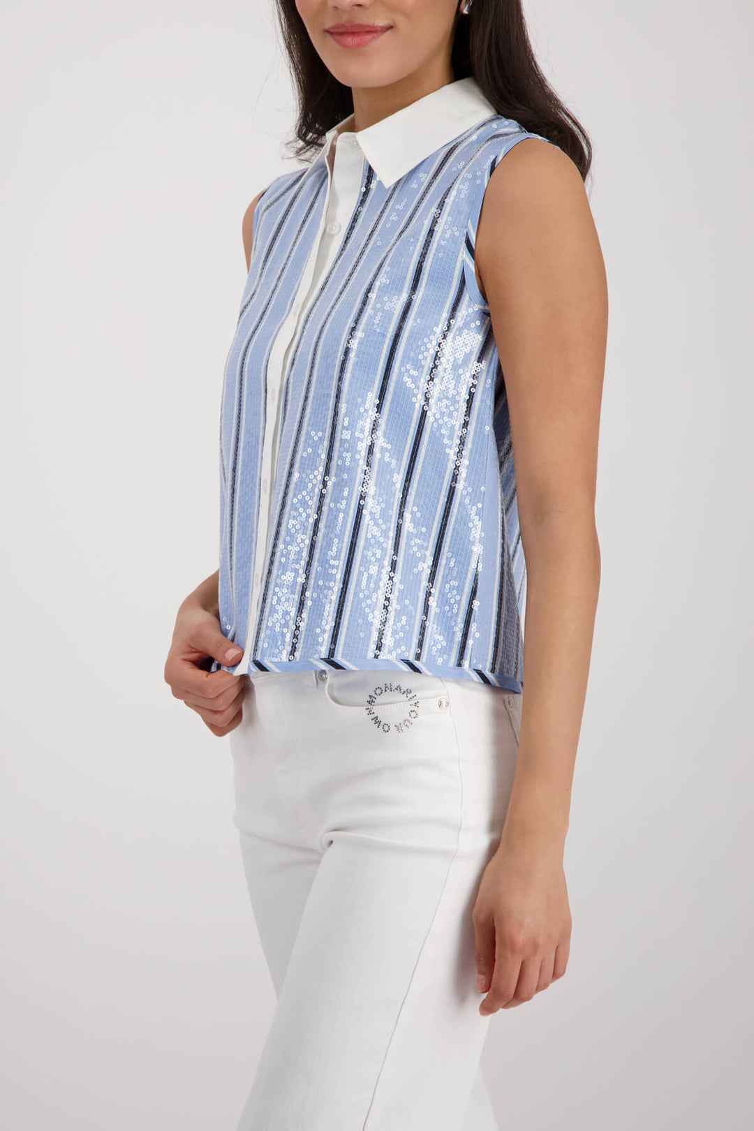 Monari woman modeling a sleeveless button-front top with vertical blue and white stripes, a white collar, and white pants against a light gray studio background.