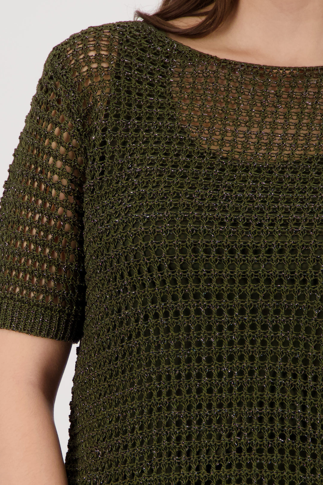 Monari  modeling a short-sleeve olive green knit top paired with white wide-leg pants featuring a green palm tree print, set against a plain light gray studio background. Close up