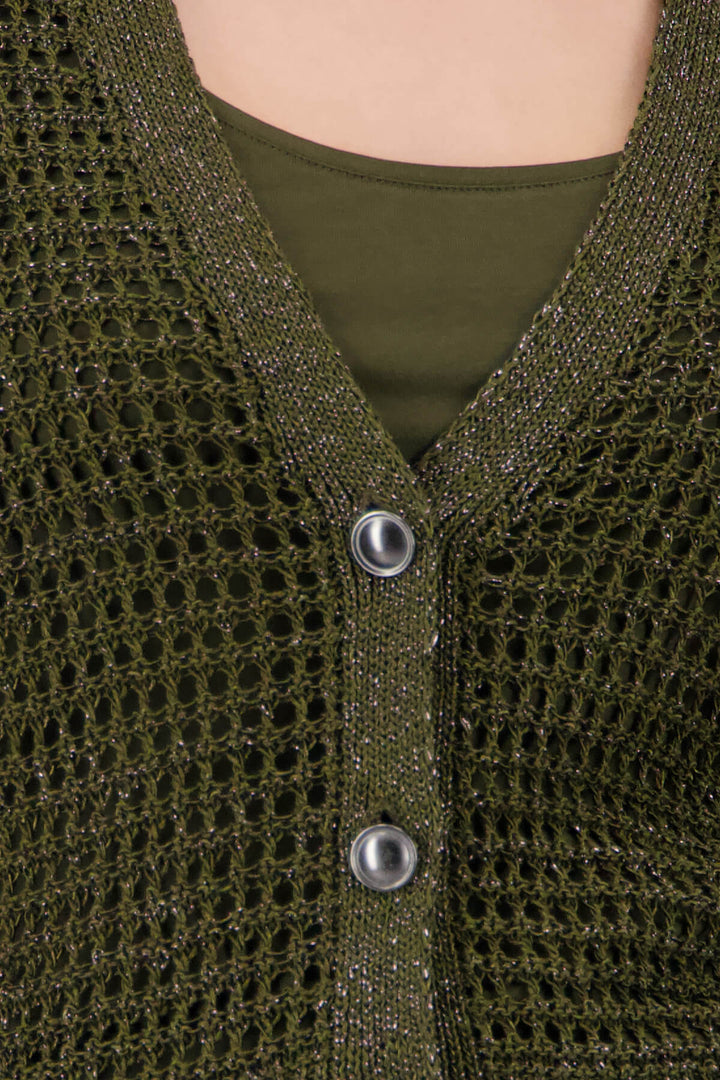 Monari woman modeling a short-sleeve olive green knit cardigan over a matching olive green top, paired with wide-leg white pants featuring a green and beige palm tree print, against a light gray studio background. Close up