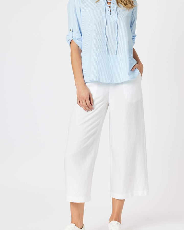Gordon Smith Model A woman modeling a light blue long-sleeve blouse with a lace-up neckline and white cropped pants, standing against a plain white studio background.