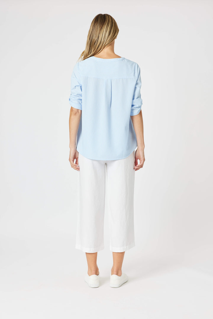 Gordon Smith Model A woman modeling a light blue long-sleeve blouse with a lace-up neckline and white cropped pants, standing against a plain white studio background.