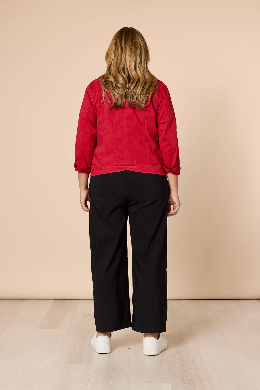 Threadz Model A woman modeling a red button-up shirt jacket over a white t-shirt and black wide-leg trousers, standing against a solid beige studio background.