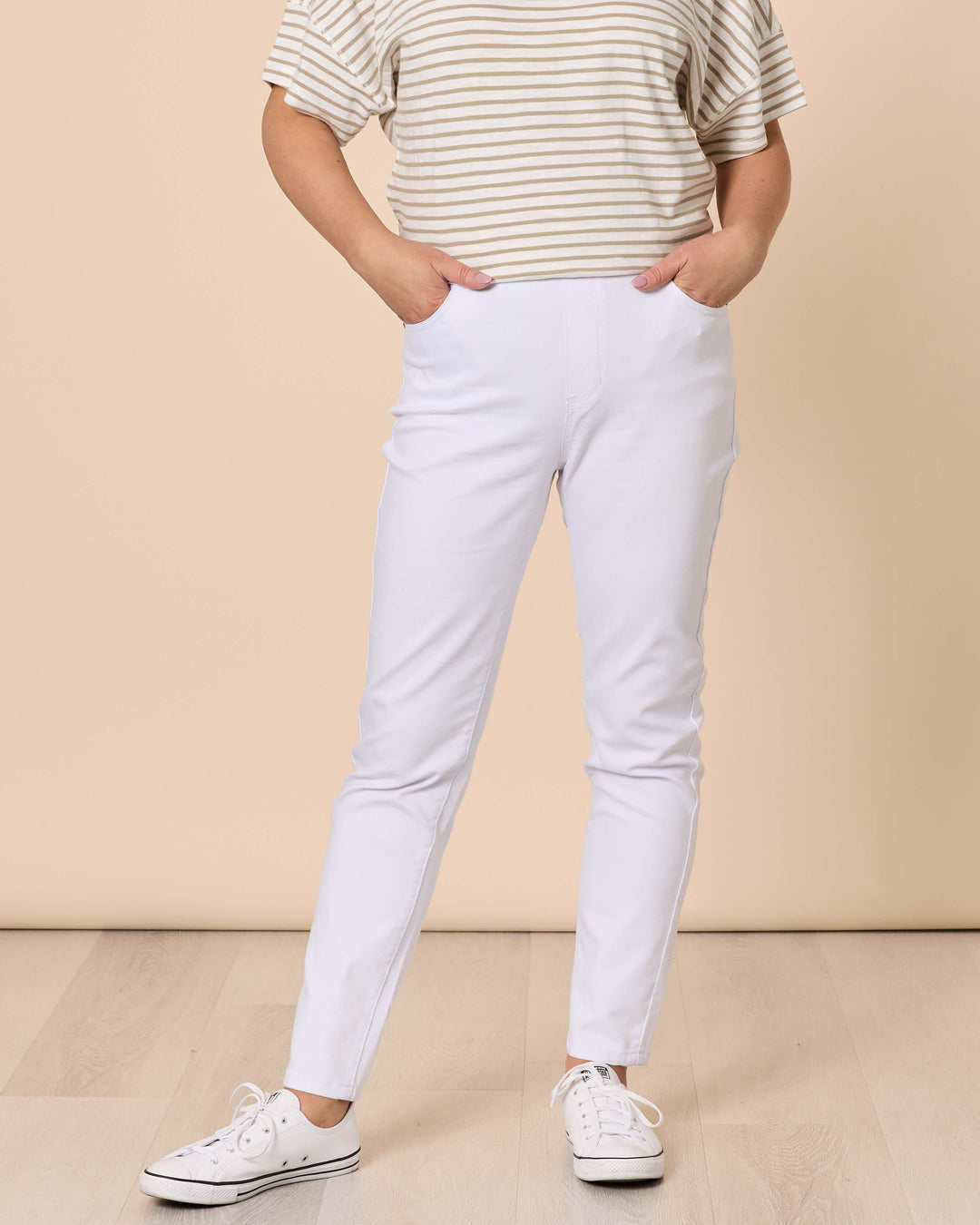 Threadz woman modeling a short-sleeve striped t-shirt and white slim jean, standing against a solid beige studio background.