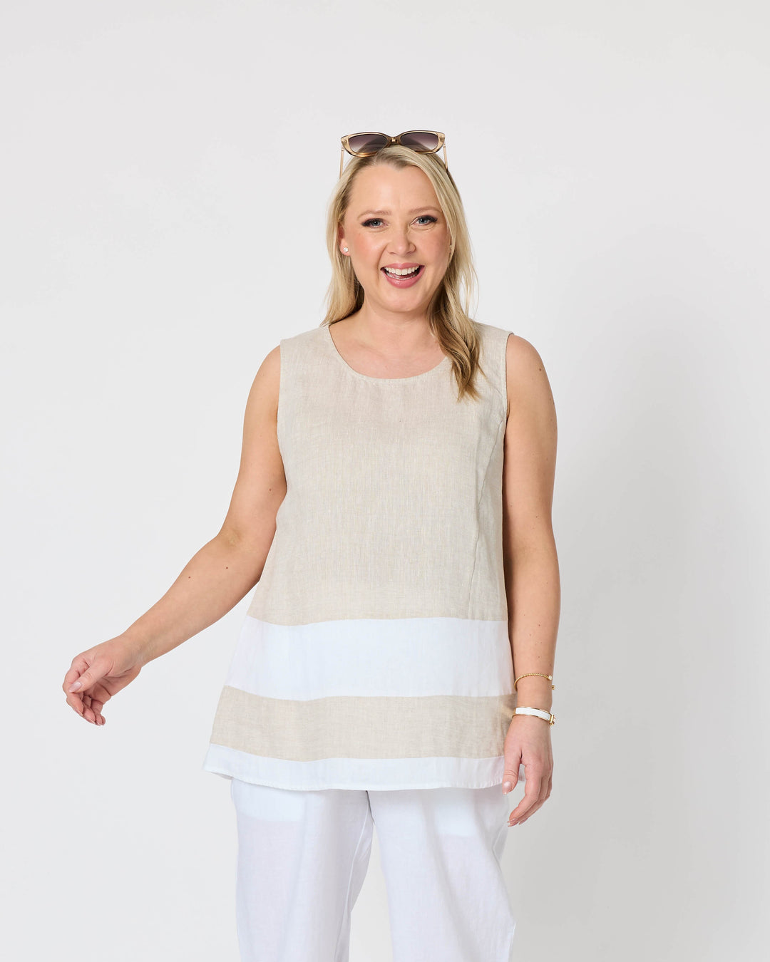 Gordon Smith woman modeling a sleeveless beige and white striped tunic top with white pants, standing against a plain light gray studio background.