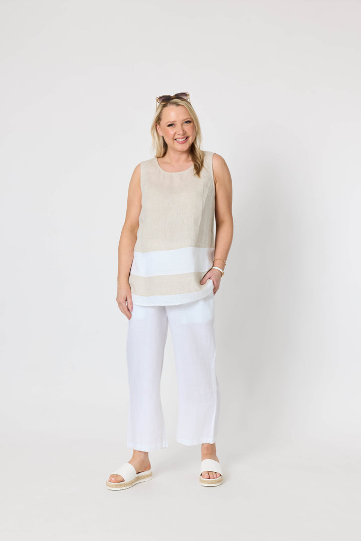 Gordon Smith woman modeling a sleeveless beige and white striped tunic top with white pants, standing against a plain light gray studio background.