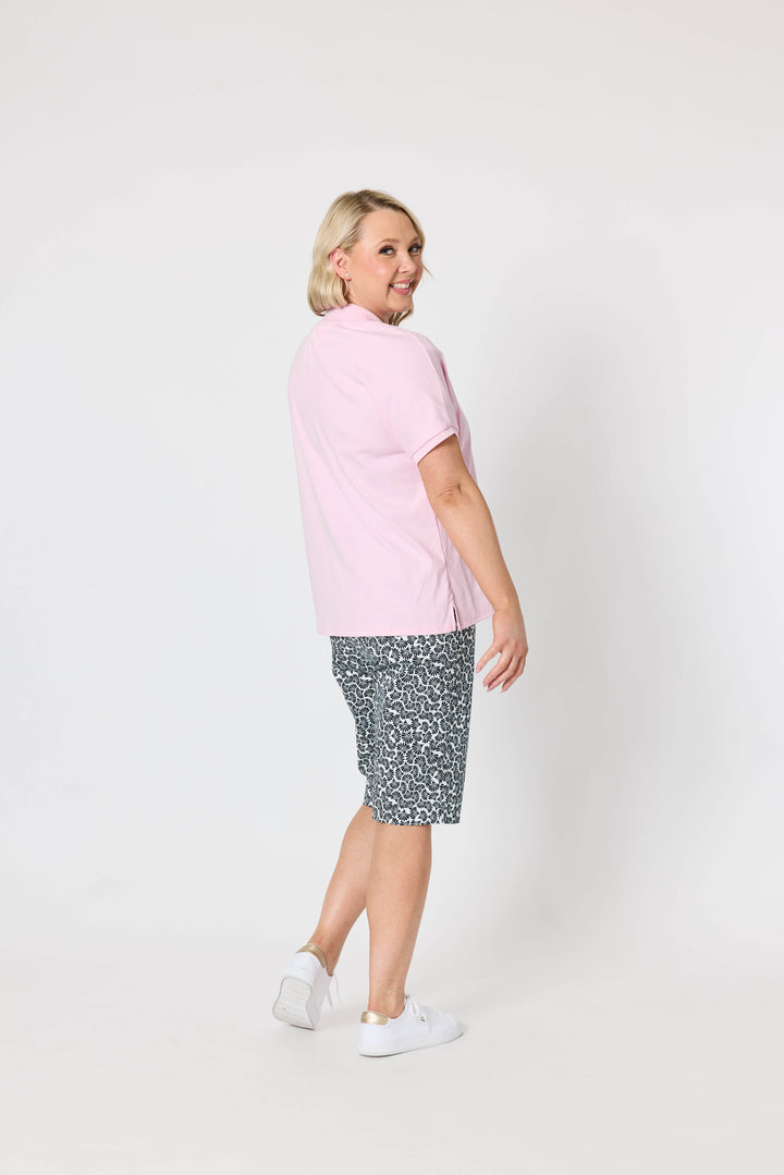 Gordon Smith Model A woman modeling a light pink short-sleeve polo shirt and dark gray and white patterned shorts against a plain white studio background.