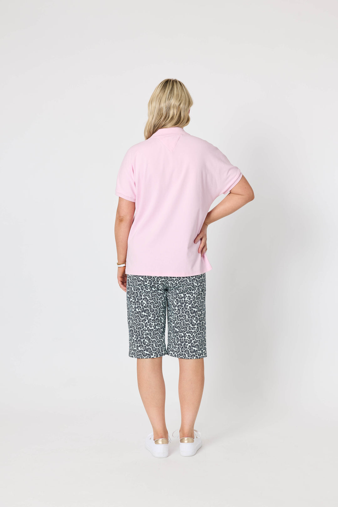Gordon Smith Model A woman modeling a light pink short-sleeve polo shirt and dark gray and white patterned shorts against a plain white studio background.