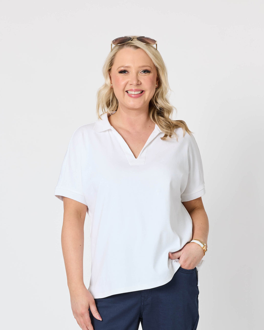 Gordon Smith Model A woman modeling a white short-sleeve polo shirt and navy blue cropped pants against a plain light gray studio background.