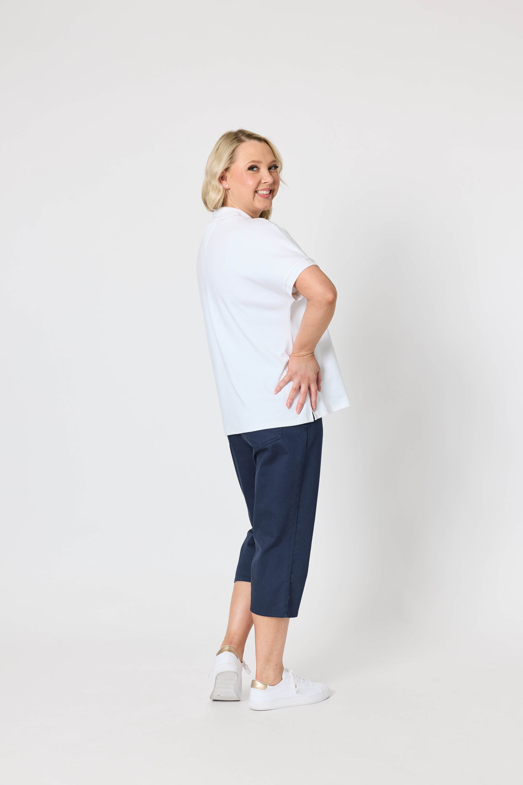 Gordon Smith Model A woman modeling a white short-sleeve polo shirt and navy blue cropped pants against a plain light gray studio background.